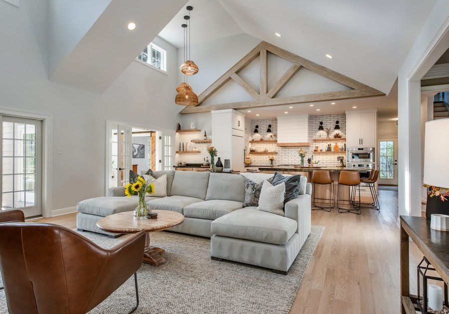 Renovated open-plan living room with vaulted timber trusses, a sectional sofa and an open kitchen beyond
